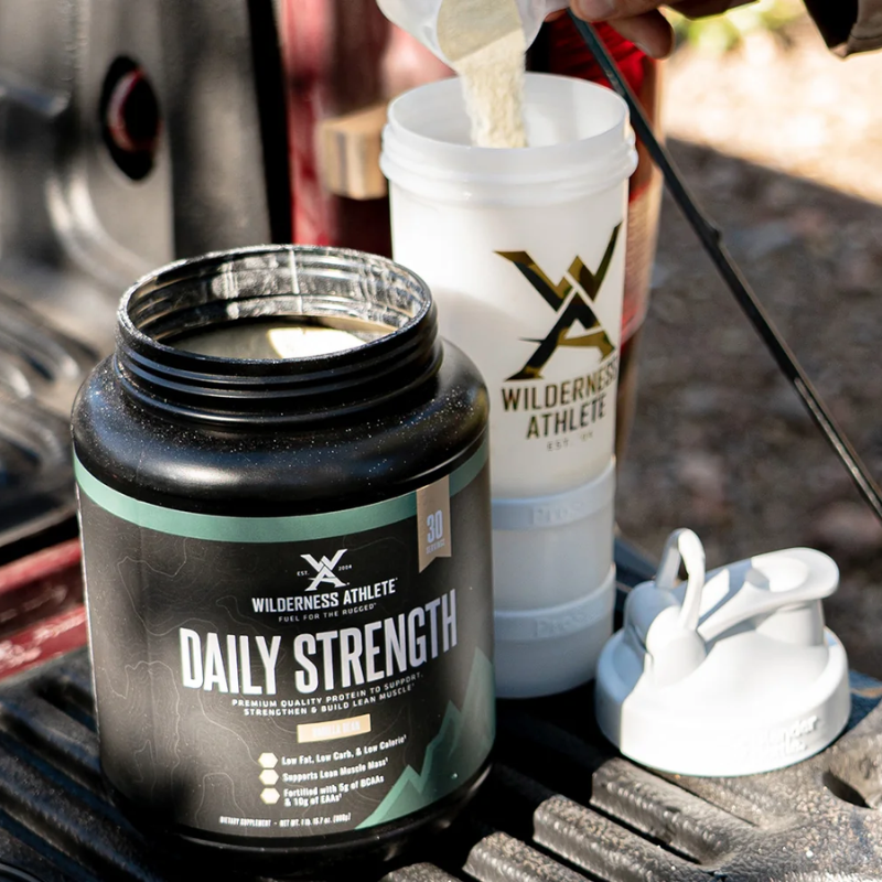 Wilderness Athlete Daily Strength supplement with a scoop and container on a camping stove.