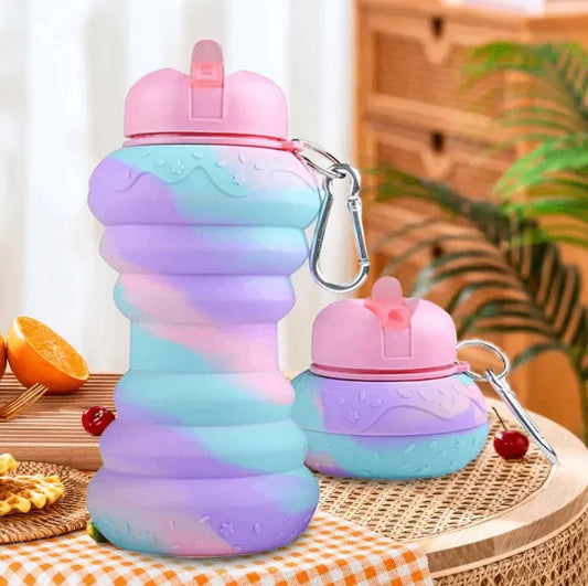 Collapsible water bottle with colorful gradient design on a wooden surface with a plant in the background.