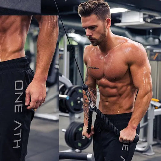Muscular man exercising with resistance bands in a gym, wearing black shorts with 'ONE ATH' branding.