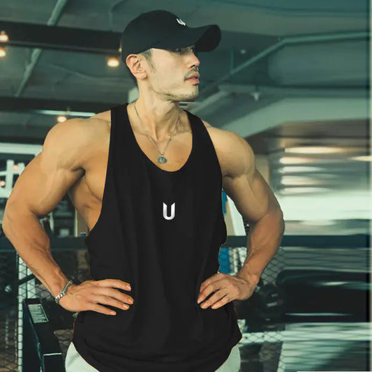 Muscular man in a black tank top with a logo, posing in a gym.
