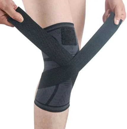 Black knee brace being worn on a person's knee with a plain background